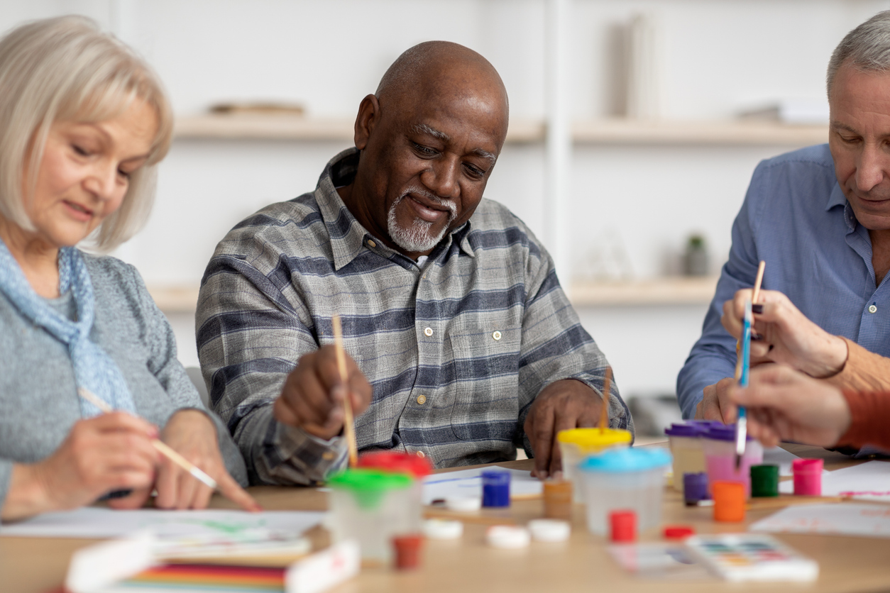 Happy multiracial elderly men and women enjoying painting with brush Art therapy for seniors concept. Happy multiracial elderly men and women enjoying painting with brush, having conversation and smiling, attending drawing master-class together