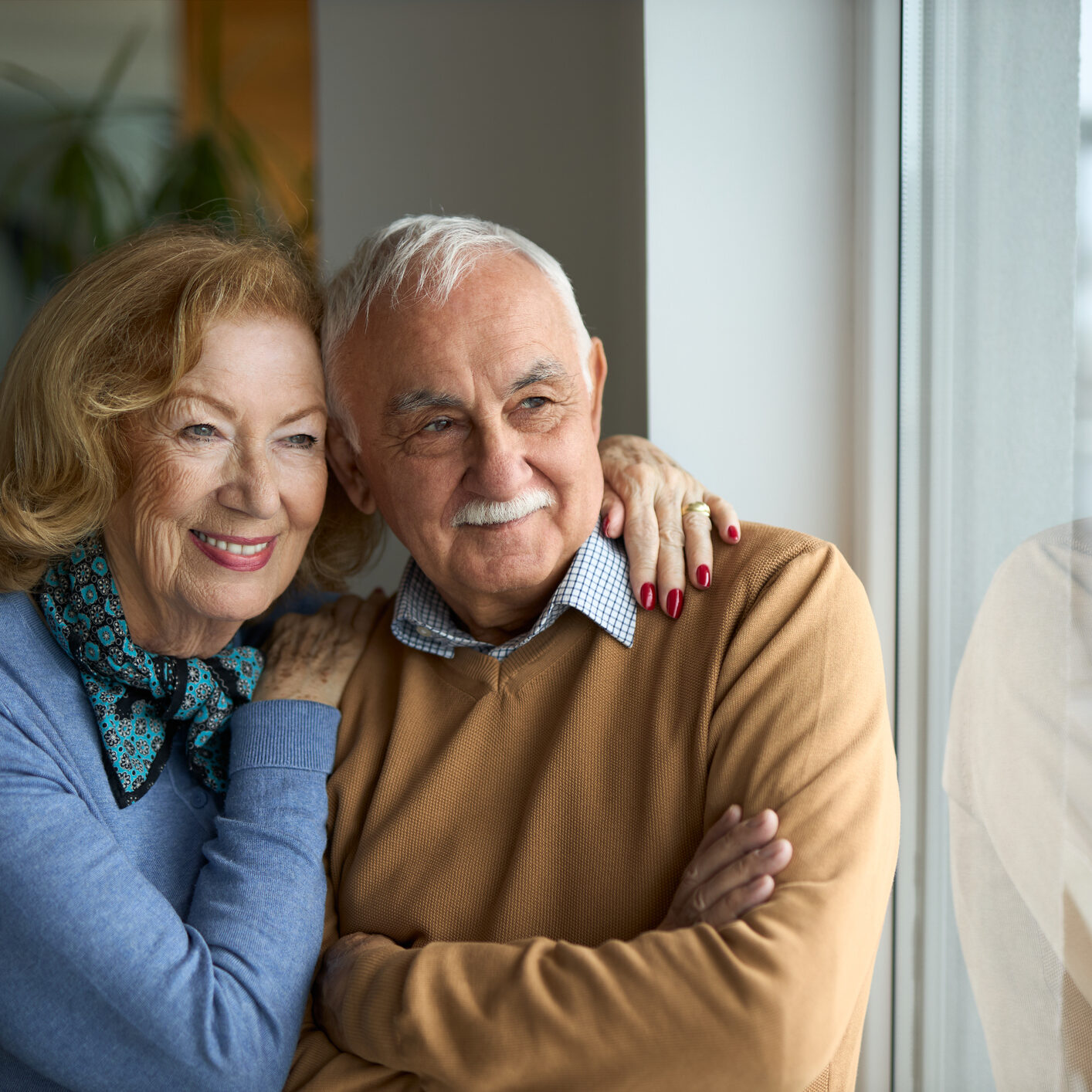 Happy mature couple looking through window at home.